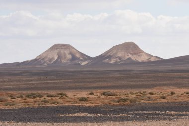 Kuru ve geniş bir arazide iki göze çarpan ikiz tepe kulesi, parçalı bulutlu bir gökyüzünün altında kayalık arazi ve seyrek bitki örtüsüyle karakterize edilir..