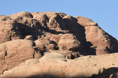 Kahverengi kumtaşı oluşumları mavi gökyüzüne çarpıcı bir şekilde yükselir, sakin bir çöl manzarasında gün ortasında doğal heykel benzeri yapılar sergilerler..