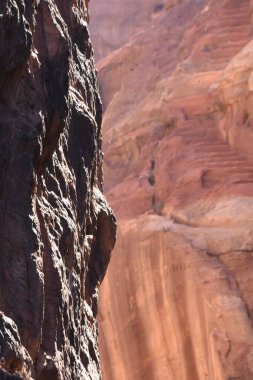 Sahne, güneş ışığıyla aydınlatılan bir kanyonda canlı kaya katmanları sergiliyor. Koyu ve kırmızımsı renklerin kontrastı çarpıcı bir görüntü yaratır. Doğanın sanatı burada sergileniyor..