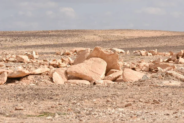 Kurak bir arazi, açık mavi bir gökyüzünün altında, yeryüzündeki erozyon şekillerini ortaya çıkaran, dağılmış kaya ve taşları barındırır. Kuru, kayalık zemin arka planda durmaksızın uzanıyor..
