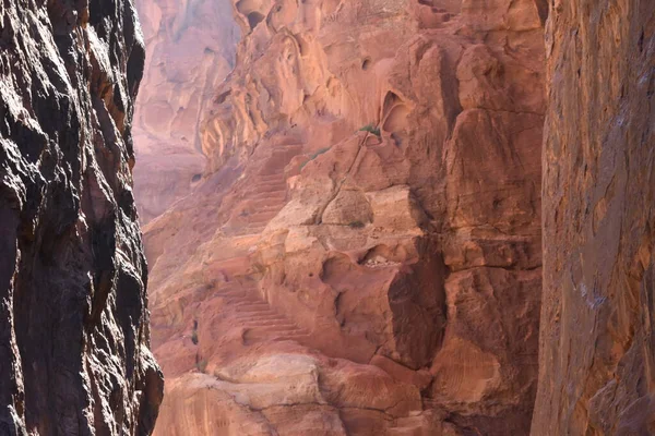 Derin kanyon, çarpıcı kırmızı kaya oluşumlarını ve dik doğal basamakları ortaya çıkarır. Güneş ışığı canlı manzarayı aydınlatır, doğanın güzelliğini nefes kesici bir şekilde gösterir..