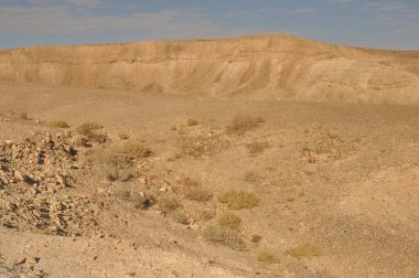 Kuru bir çöl manzarası, kayalık zemin ve minimum bitki yaşamı. Manzara, bu uzak bölgenin çorak güzelliğini vurgulayan tepeler ve geniş bir gökyüzü barındırıyor..