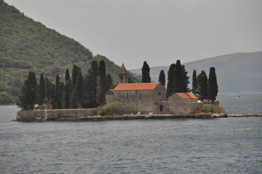 Sakin bir adada uzun selvi ağaçları ile çevrili bir taş kilise bulunur. Sahne, Adriyatik Denizi 'nin yeşil dağlarıyla güzelliğini yakalıyor..