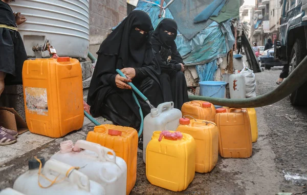Taiz / Yemen - 28 Haziran 2020: Yemenli bir kadın Yemen 'in Taiz kentinde devam eden savaş nedeniyle su arayışı içinde ve litrelerce su dolduruyor 