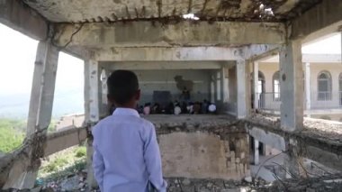 Taiz Yemen - 07 Ekim 2020: Savaş tarafından yıkılan bir okulun içindeki Yemenli bir çocuk içeride okuyan sınıf arkadaşlarına bakıyor