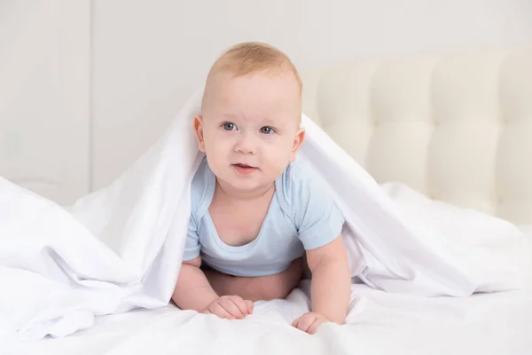 Engraçado bebê menino sorrindo e deitado em uma cama branca em casa. — Fotografia de Stock