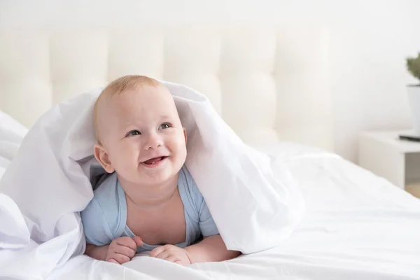 Funny baby boy smiling and lying on a white bedding at home. — Stock Photo, Image