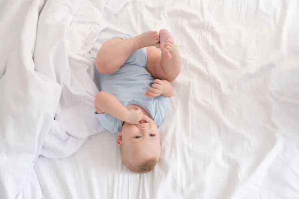 Funny baby boy lying on bed at home on white bedding. top view. — Stock Photo, Image