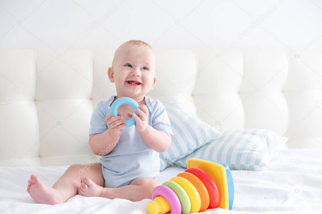 funny baby boy sits on bed and play with a toy childrens pyramid.