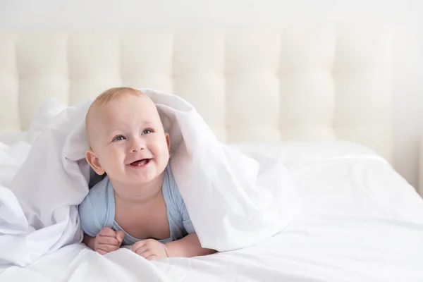 Смешной мальчик улыбается и лежит на белом постельном белье дома. — стоковое фото