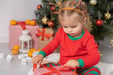 Noel ağacının yanında boynuzları geyik boynuzlu küçük kız hediyesini açıyor..