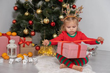 Noel ağacının yanında boynuzları geyik boynuzlu küçük kız hediyesini açıyor..