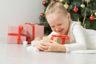 Noel ağacının yanında elinde hediye kutusuyla yerde yatan tatlı küçük kız..