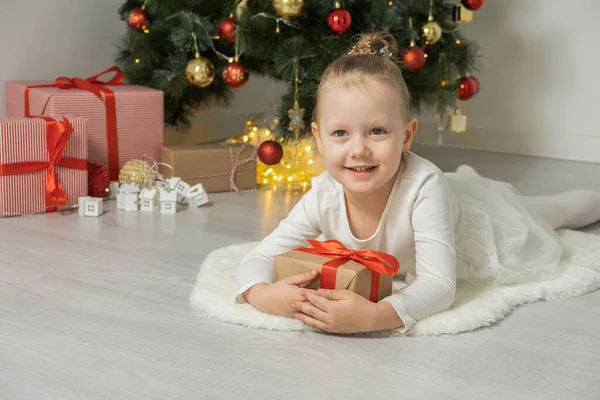 Cute little child girl lying on the floor near the Christmas tree with gift box. — Stock Photo, Image