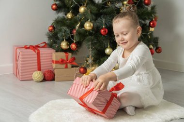 Neşeli şirin kız çocuklar hediye kutusunu açıyor Noel ağacının yanında beyaz elbiseler içinde eğleniyorlar..