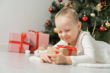 Noel ağacının yanında elinde hediye kutusuyla yerde yatan tatlı küçük kız..