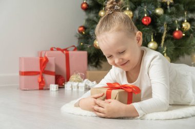 Noel ağacının yanında elinde hediye kutusuyla yerde yatan tatlı küçük kız..