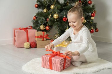 Neşeli şirin kız çocuklar hediye kutusunu açıyor Noel ağacının yanında beyaz elbiseler içinde eğleniyorlar..