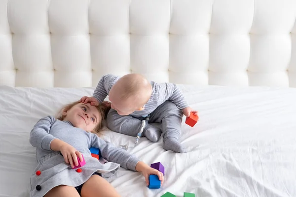 Menino e menina irmã brincando de brinquedos de madeira em casa na cama. Atividades domésticas para crianças. — Fotografia de Stock