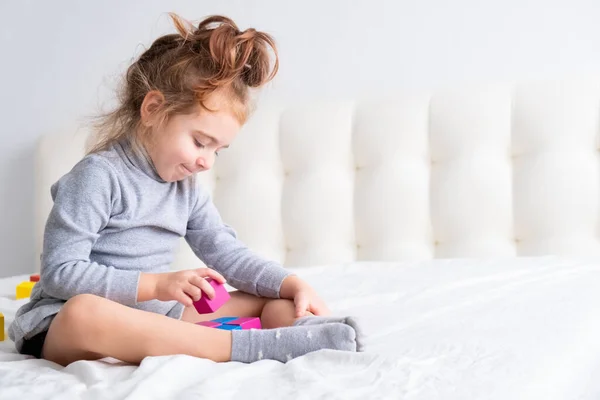 Menina brincando com cubos de madeira coloridos sentados na cama. Atividades domésticas para crianças. — Fotografia de Stock