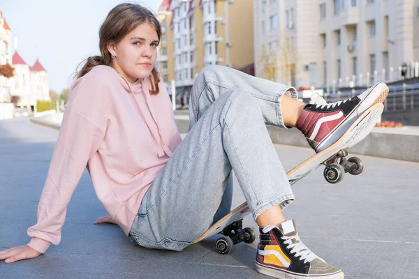 Mladý alternativní teenager dívka bruslař sedí na palubě na ulici města dívá pryč. — Stock fotografie