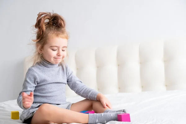 Menina bebê brincando de brinquedos de madeira em casa na cama. Atividades domésticas para crianças. — Fotografia de Stock