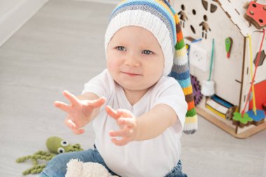 Komik şapkalı, beyaz tişörtlü, evde oyuncak ayıyla oynayan bebek..