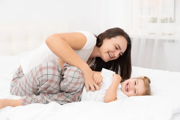 Volwassen moeder is kietelen haar kleine actieve dochter thuis, plezier hebben, activiteit met kinderen. — Stockfoto