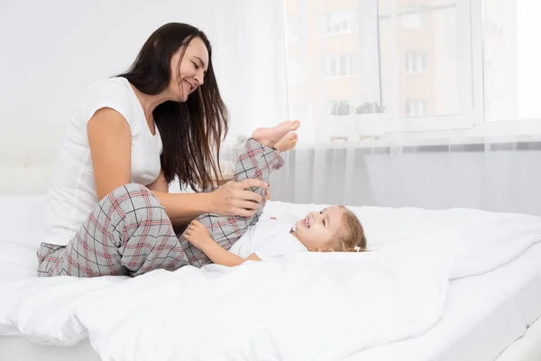 Доросла мати грає з маленькою активною дочкою в ліжку вдома, розважається, займається з дітьми . — стокове фото