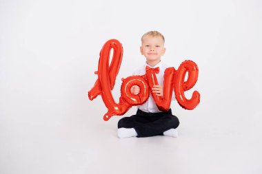 Takım elbiseli çocuk ve kırmızı papyonlu çocuk balonların beyaz arka plandaki yazıtlarını tutuyor.