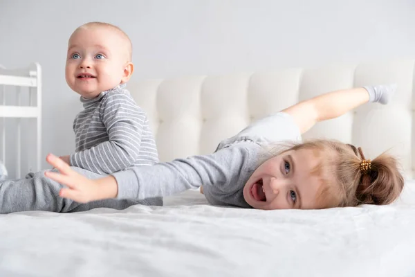 Mały chłopiec i mała siostrzyczka bawią się w domu w łóżku. Home zajęcia dla dzieci. — Zdjęcie stockowe