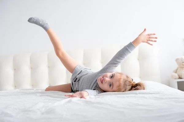 Menina em gola alta cinza se divertindo na cama branca — Fotografia de Stock