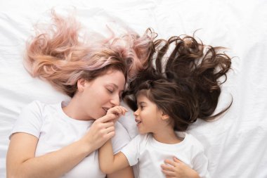 Genç anne ve küçük aktif kız yatakta uzanıp eğleniyorlar.
