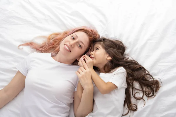 young mother and little active daughter lying in bed at home, having fun