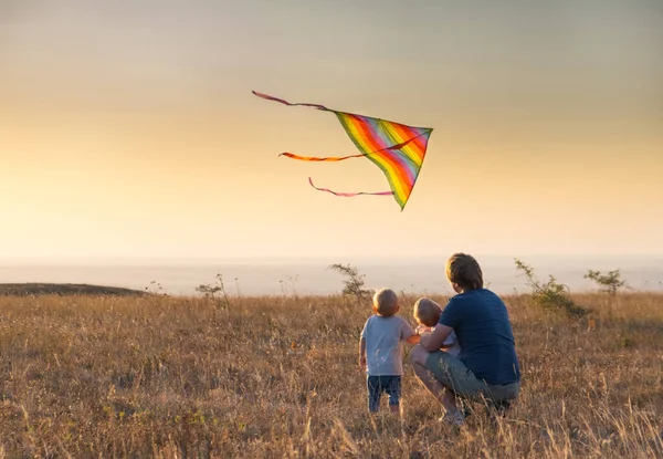 dad and kids boys fly a kite at sunset