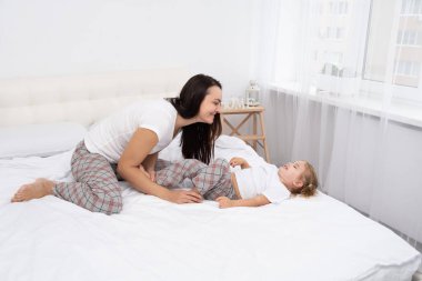 Yetişkin anne, aktif kızını evde yatakta gıdıklıyor. Çocuklarla boş vakit geçiriyor.