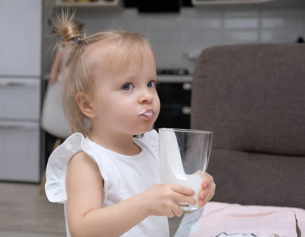 かわいい金髪の女の子がオーガニックミルクを飲み家のキッチンでガラスを持ち — ストック写真