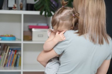 Küçük kızını kollarında kucaklayan ve teselli eden genç bir anne. Ebeveyn sevgisi ve sevgisi