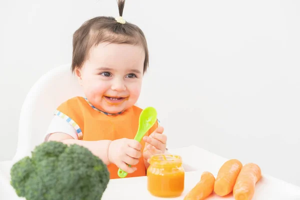 Dziewczynka Pomarańczowym Śliniaczka Siedzi Fotelu Childs Jedząc Puree Warzywne Białym — Zdjęcie stockowe