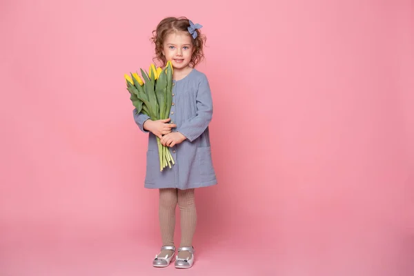 Pembe arka planda sarı lale demeti olan mavi elbiseli güzel sarışın kız..