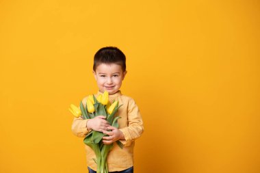 Sarı stüdyo arka planında gülümseyen küçük çocuk. Lale çiçekli neşeli çocuk..