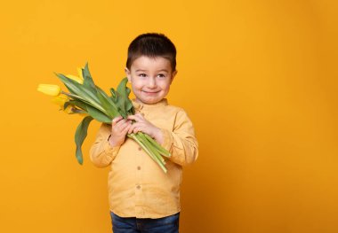 Sarı stüdyo arka planında gülümseyen küçük çocuk. Lale çiçekli neşeli çocuk..
