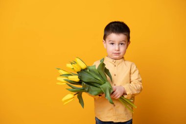 Sarı stüdyo arka planında gülümseyen küçük çocuk. Lale çiçekli neşeli çocuk..