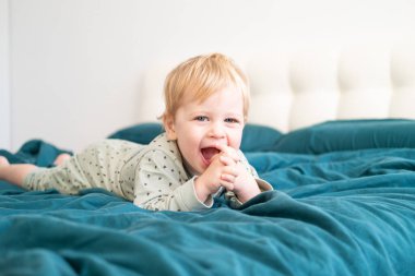 Yeşil pijamalı küçük sağlıklı çocuk evde yatakta uzanıp eğleniyor..