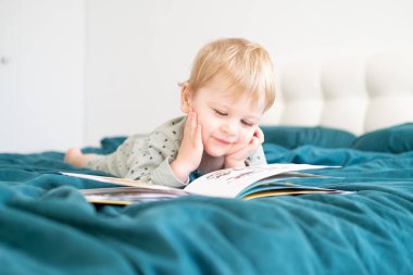 Pijamalı küçük mutlu çocuk ailesinin yatağında kitap okuyor..