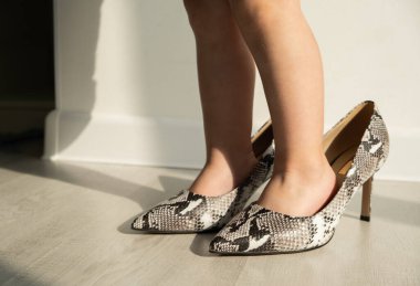 Güneşli bir öğleden sonra annesinin ayakkabılarını deneyen küçük kızın bacaklarını kapat..