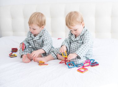 İki komik erkek kardeş beyaz yatakta pijamalı ikizler manyetik yapıcı ile oynuyorlar.