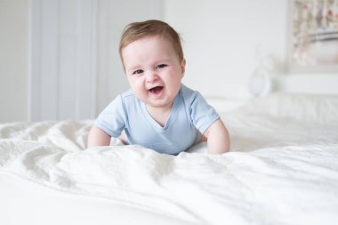 6 aylık mavi elbiseli komik bir bebek. Gülümsüyor ve evde yatakta yatıyor.