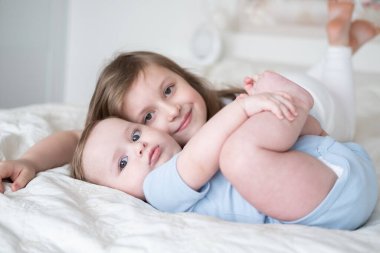 girl older sister hugging her little baby boy brother on bed at home.