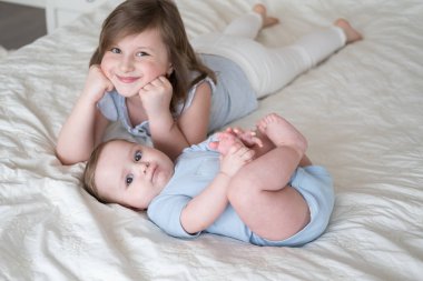 girl older sister lying on bed with her little baby boy brother at home.